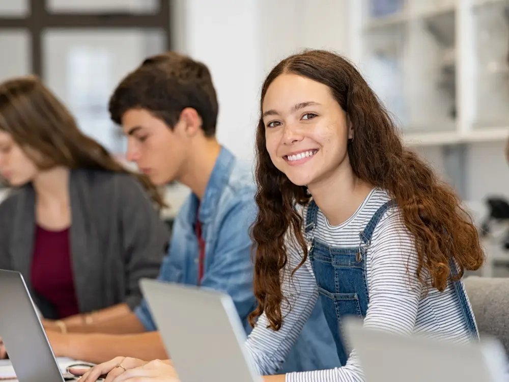 Estudiante universitaria sonriente en clase, frente a su laptop