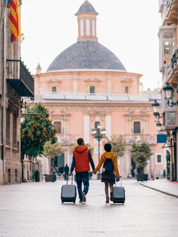 Pareja joven de viaje con maletas en una plaza europea: en la primera etapa el sueldo se va en experiencias y el retiro ni siquiera aparece en el radar